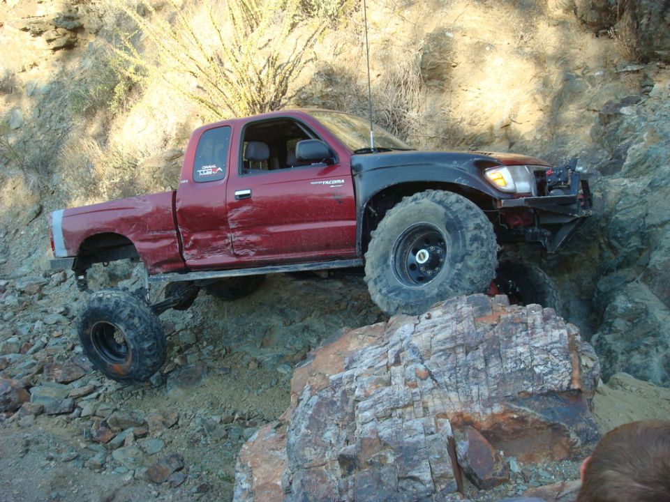 Red Toyota Tacoma with black fender flares climbing over rocks on a trail