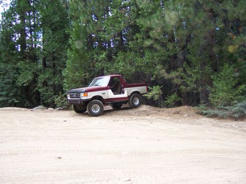 1991 Ford Bronco - Maroon and white 1991 Ford Bronco parked on a dirt track near a forest.
