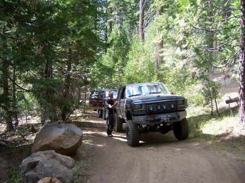 1991 Ford Bronco - Two trucks drive down a dirt road in a forest.