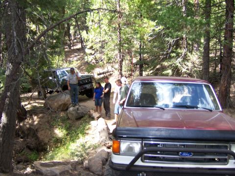 1991 Ford Bronco - A red 1991 Ford Bronco is seen off-road with a group of people and another vehicle in the background.