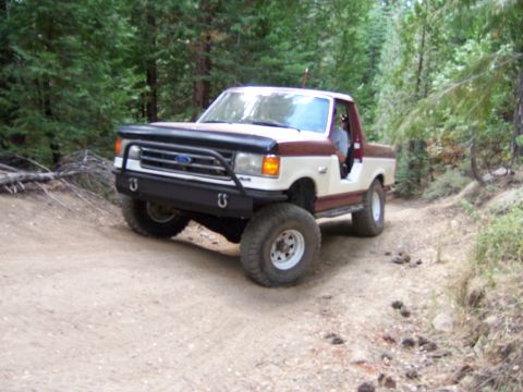 1991 Ford Bronco - A 1991 Ford Bronco navigates a wooded trail with its front end angled towards the camera.