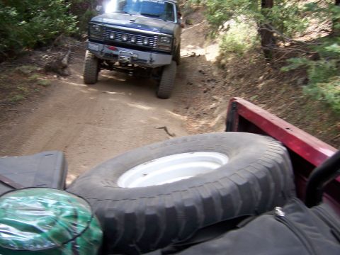 1991 Ford Bronco - A 1991 Ford Bronco navigates a dirt road, seen from the perspective of another vehicle's bed.
