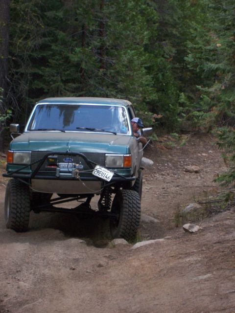 1991 Ford Bronco - Modified pickup truck navigates a rocky trail surrounded by trees.