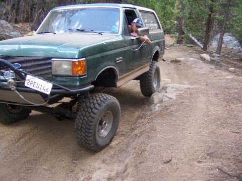 1991 Ford Bronco - A green 1991 Ford Bronco navigates a rocky off-road trail, demonstrating its capability on challenging terrain.