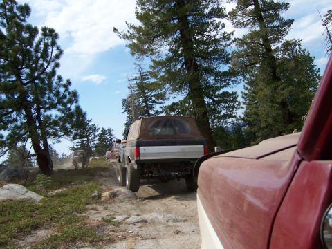 1991 Ford Bronco - A convoy of off-road vehicles navigates a dusty trail through a wooded, mountainous area.