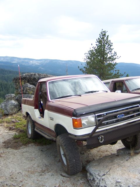 1991 Ford Bronco - A two-tone Ford Bronco is parked on rocky terrain with a scenic mountain view in the background.