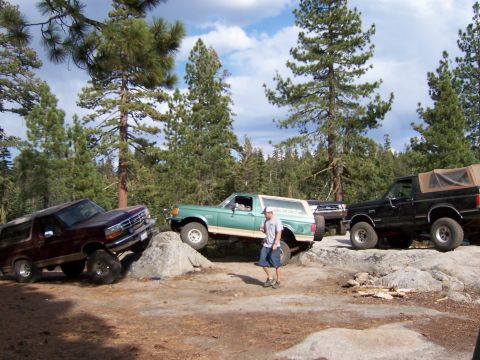 1991 Ford Bronco - Three Ford Bronco SUVs are shown off-roading on a rocky trail.