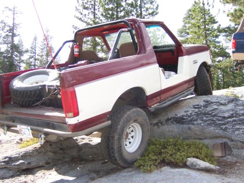1991 Ford Bronco - A two-tone red and white 1991 Ford Bronco navigates rocky terrain with a spare tire mounted in the cargo area.