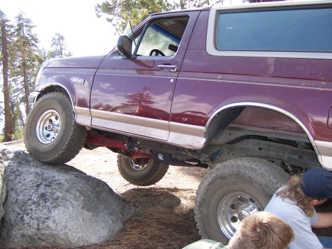 1991 Ford Bronco - This maroon Ford Bronco is shown from the side, with its front tire on a large rock, indicating off-road use.