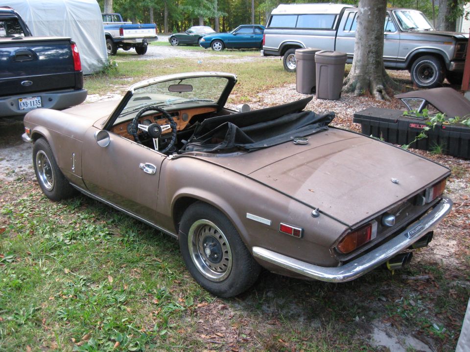 Brown Triumph Spitfire convertible parked on grass, other trucks in background