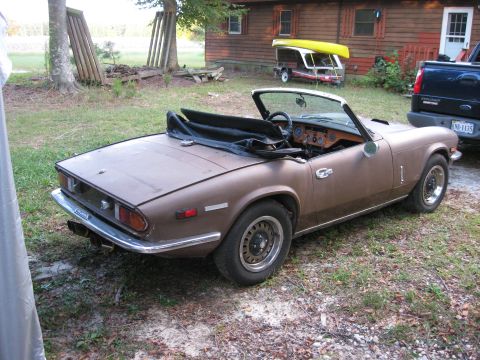 1991 Ford Bronco - A brown Triumph Spitfire convertible sits in a grassy yard next to a wooden building.