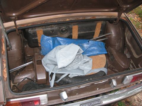 1991 Ford Bronco - The trunk of a brown car contains a spare tire, fuel tank, and covered items.