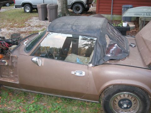 1991 Ford Bronco - A brown convertible with a black soft top is parked outdoors, with other vehicles and trash cans visible in the background.