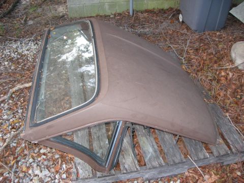 1991 Ford Bronco - A brown car hardtop with glass windows rests on weathered wooden planks amidst fallen leaves and debris.