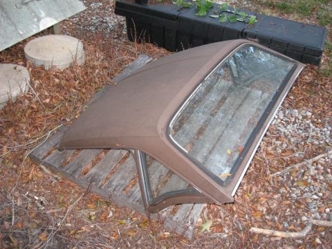 1991 Ford Bronco - A brown car hardtop sits on wooden planks amidst fallen leaves and debris.