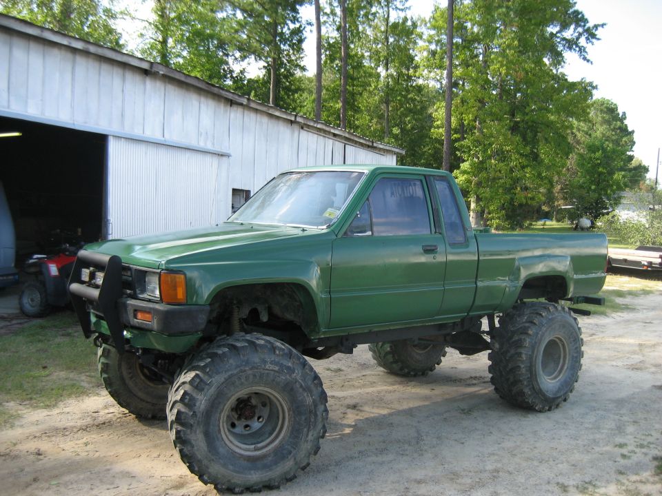 Lifted green Toyota extended-cab pickup on large mud tires by a barn