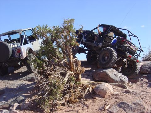 1986 Ford Bronco II - Two modified off-road vehicles tackle a challenging rocky trail under a clear blue sky.