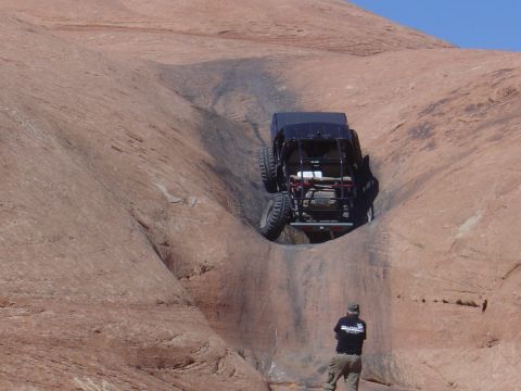 1986 Ford Bronco II - A black off-road vehicle navigates a challenging ascent on a rocky terrain, with a spectator observing the action.