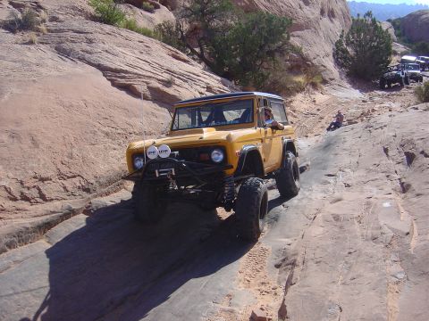 1986 Ford Bronco II - A modified yellow SUV tackles a challenging rocky terrain, with other vehicles visible in the background.