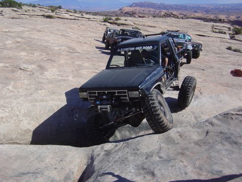 1986 Ford Bronco II - Multiple off-road vehicles navigate a rocky trail under a clear sky.