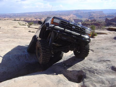 1986 Ford Bronco II - This modified SUV navigates a challenging rocky trail under a partly cloudy sky.