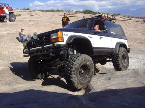 1986 Ford Bronco II - A modified 1986 Ford Bronco II navigates rocky terrain with another vehicle visible in the background.