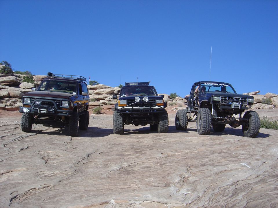 Three lifted off-road vehicles on rocky terrain