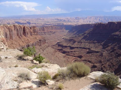 1986 Ford Bronco II - A vast canyon landscape with layered rock formations and distant mountains under a partly cloudy sky.