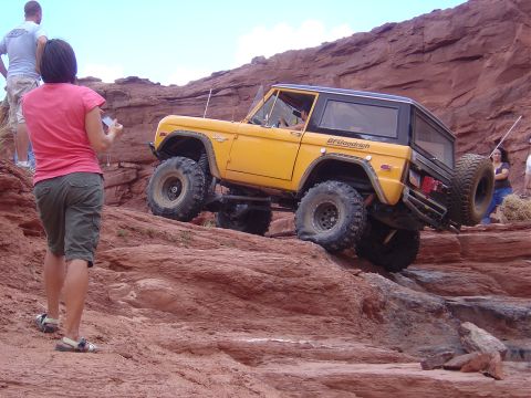 1986 Ford Bronco II - An off-road SUV navigates a steep, rocky incline with spectators observing the challenging climb.