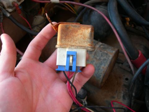1984 Ford Bronco - A hand holds a rusty electrical relay with a blue connector and attached wires, likely from a vehicle's engine bay.