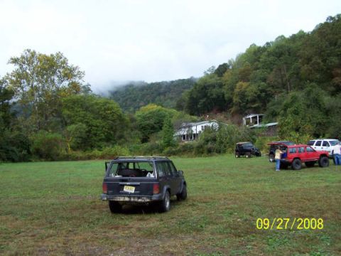 1992 Jeep Cherokee - A group of Jeep Cherokees are gathered in a field on a cloudy day, with a wooded hillside behind them.