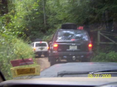 1992 Jeep Cherokee - Two SUVs drive down a wooded dirt road, one black Jeep Cherokee and a white SUV.