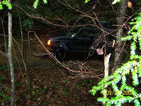1992 Jeep Cherokee - A black 1992 Jeep Cherokee navigates a muddy trail surrounded by dense forest foliage.
