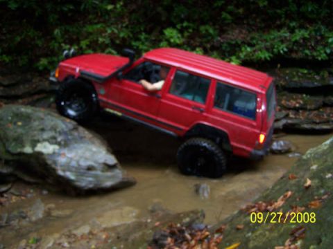 1992 Jeep Cherokee - A red 1992 Jeep Cherokee navigates a rocky, muddy off-road trail.