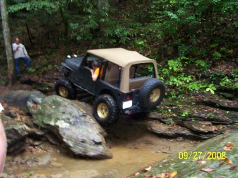 1992 Jeep Cherokee - A black Jeep Wrangler navigates a muddy off-road trail with a tan soft top and gold wheels.