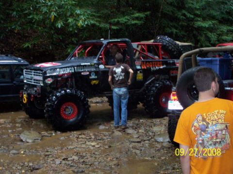 1992 Jeep Cherokee - A heavily modified off-road truck is seen on a muddy trail with other vehicles in the background.