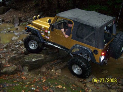 1992 Jeep Cherokee - A gold Jeep Wrangler is shown off-roading on a rocky, wet trail.