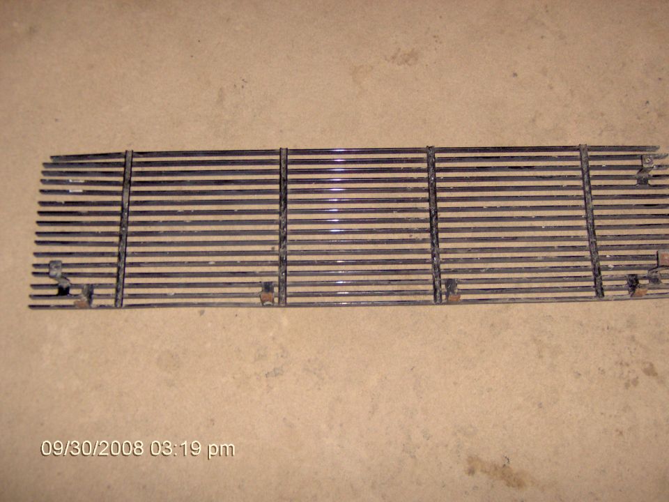 Back side of a horizontal-bar grille lying on carpet showing mounting tabs