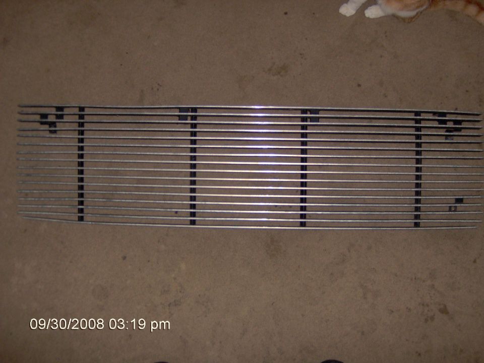 Chrome billet horizontal-bar grille lying on carpet near an orange cat