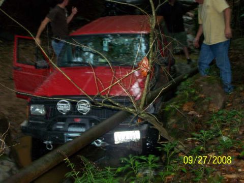 1992 Jeep Cherokee - A red 1992 Jeep Cherokee is stuck off-road, with branches obscuring the windshield and front grille.