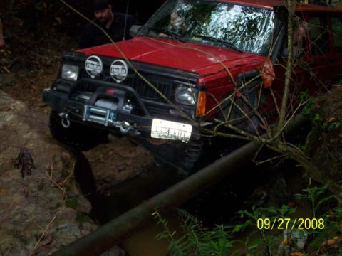 1992 Jeep Cherokee - A red 1992 Jeep Cherokee navigates a muddy trail, partially submerged in water.