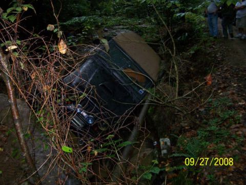 1992 Jeep Cherokee - A 1992 Jeep Cherokee is seen tilted in a ditch, partially obscured by foliage.