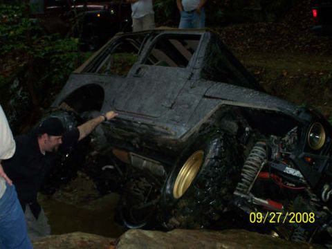 1992 Jeep Cherokee - Modified Jeep Wrangler off-roading, stuck in mud with a person reaching towards it.