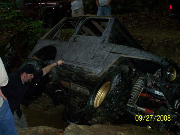 Modified Jeep Wrangler with large tires stuck in mud, driver reaching towards it. Date stamp 09/27/2008