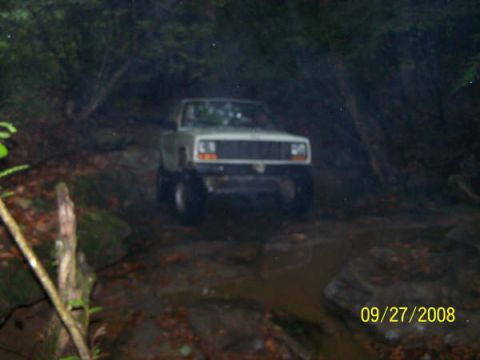 1992 Jeep Cherokee - A Jeep Cherokee navigates a wet, off-road trail surrounded by trees.