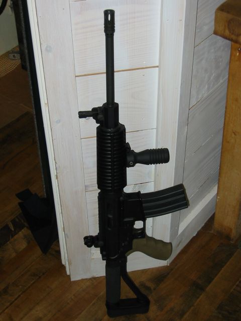 1996 Ford Bronco - A black assault rifle with a tan grip and a black magazine is shown leaning against a white wooden wall.