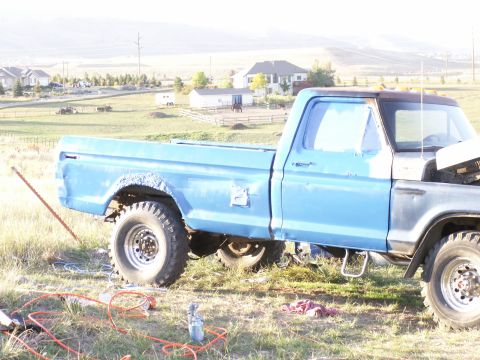 1977 Ford F-250 - A blue pickup truck is parked on a grassy area, with tools and spray paint cans nearby.