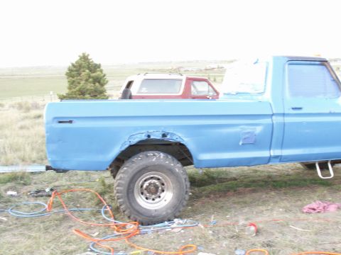 1977 Ford F-250 - A blue pickup truck with visible body damage sits outdoors next to a red SUV in its bed.