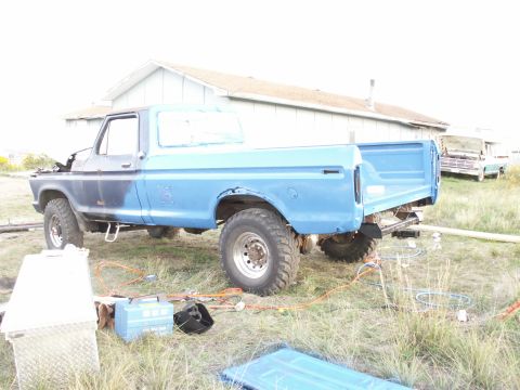 1977 Ford F-250 - This 1977 Ford F-250 pickup truck is seen from the rear three-quarter angle, parked in a grassy area with another vehicle in the background.
