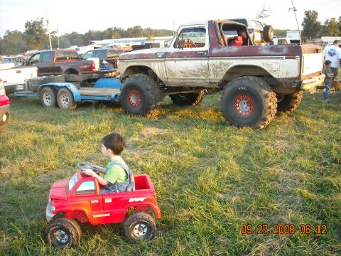 1979 Ford Bronco - A modified off-road vehicle sits in a grassy field with a child in a toy car in the foreground.